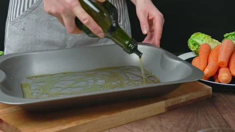Adding oil into an oven pan from a bottle and brushing with a brush in 4k. Stock Footage 145114570