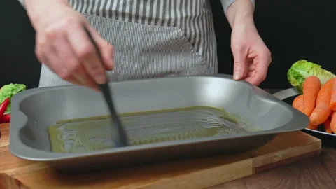 Adding oil into an oven pan from a bottle and brushing with a brush in 4k. Stock Footage 145114791