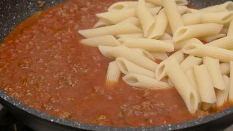 Adding penne pasta into boiling bolognese sauce in a frying pan 库存影片 289683741