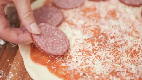 Adding pepperoni on top of a pizza dough. Concept of preparation in 4K. Stock Footage 137430835