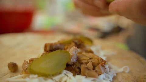 Adding pickled cucumbers to meat and cheese on pita bread, close-up Stock Footage 311403875