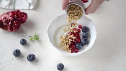 Adding pine nuts into Greek yogurt with blueberry and pomegranate Video stock 165822656