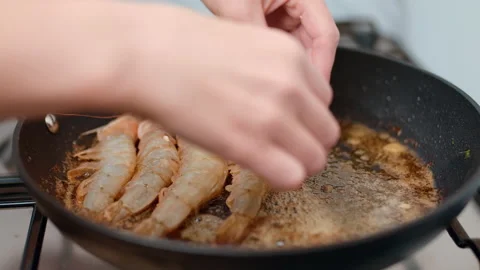 Adding, placing into a pan a bunch of shrimps/prawns and frying in butter in 4K Stock Footage 138286973