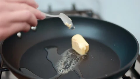 Adding, placing pieces of butter into a preheated pan on a gas stove in 4K. Stock Footage 138285942