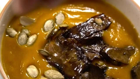Adding pumpkin seeds into bowl with pumpkin cream soup - white mushroom Stockbeeldmateriaal 141992421