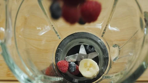 Adding raspberries, blueberries and bananas to a blender to make a smoothie Stock Footage 295063446