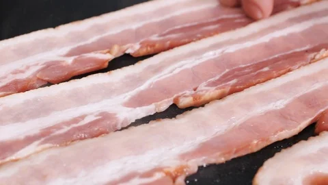 Adding raw bacon slices unto hot stove 스톡 동영상 102606664