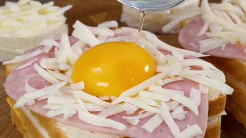 Adding raw egg yolk on top of grated cheese and ham sandwich in kitchen Stock Footage 324943339
