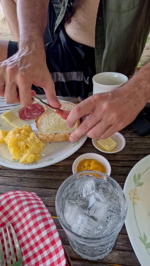 Adding salami on a slice of buttered bread on a wooden table at the beach Stock Footage 326083757
