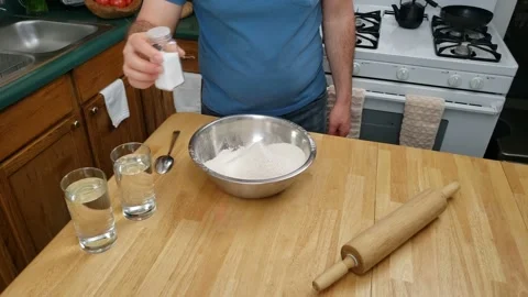 Adding salt and water into bowl of flour and mixing mixture making dough Video stock 159440435