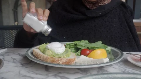 Adding salt to avocado toast with poached egg and feta cheese on plate. Stock Footage 331914250