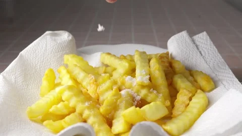 Adding salt on Crinkle Cut French Fries on a paper towel Stock Footage 333485815