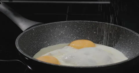 Adding salt to fried eggs, easy breakfast, black background. Close-up, slow Stock Footage 250217662