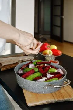 Adding salt or pepper from hand mill to vegetables in a frying pan Stock Photos