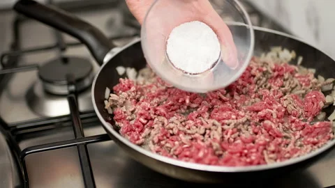 Adding salt in a preheated frying pan with chopped onion and  ground beef. Stock Footage 135462493