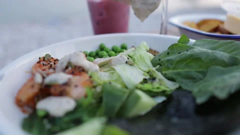 Adding sauce to a fresh salad with vegetables and salmon in an outdoor cafe Stock Footage 218165915