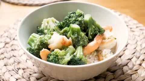 Adding shrimp and broccoli to bowl of white rice cozy kitchen table day closeup Stock Footage 128214570