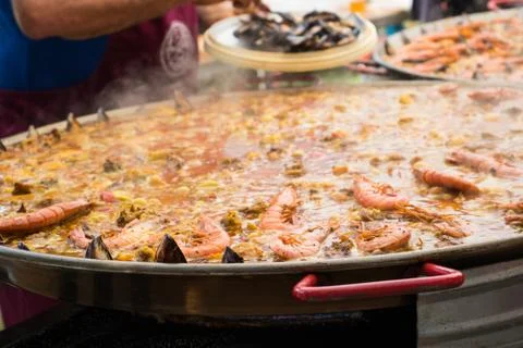 Adding shrimp and shellfish to a giant paella during cooking. Stock Photos