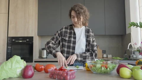 Adding Sliced Cucumber Into Bowl With Fresh Vegetable Salad In Bright Kitchen Stock Footage 308455501