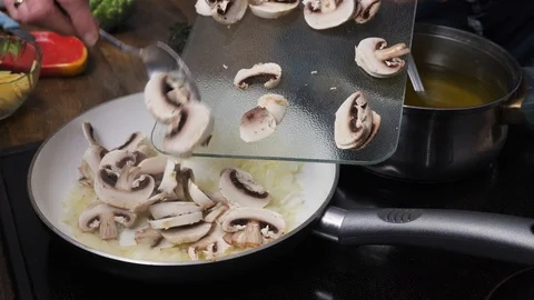 Adding sliced mushrooms into a frying pan with onions Stock Footage 88110972