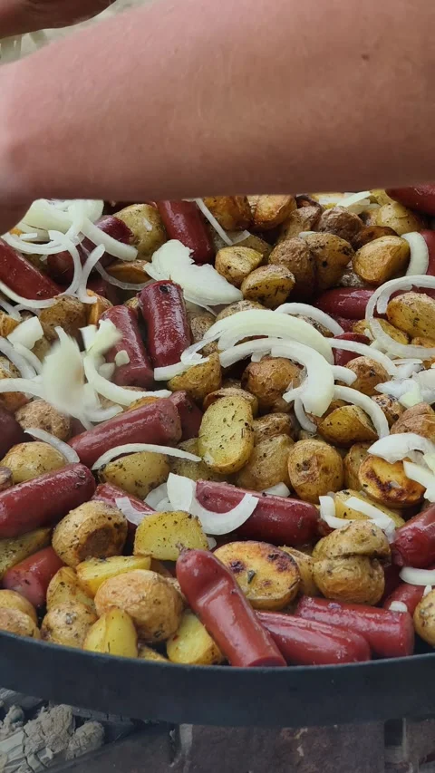 Adding Sliced Onions to Potatoes and Sausages on a Grill Stock Footage 314765238