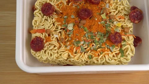 Adding smoked sausages to dry Instant noodles in a bowl rotate on wooden Vidéo 244815027