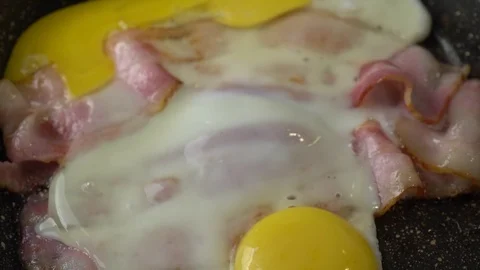 Adding some spices in a pan with two strips of bacon and two eggs Stock Footage 125930834