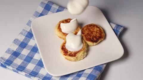 Adding sour cream to cheese pancakes. Tasty breakfast on a white plate with a Stock Footage 304681760