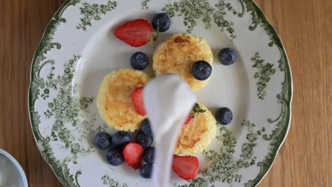 Adding sour cream to syrniki with berries on a plate Vídeo Stock 311021802