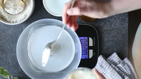 Adding sourdough starter to water in bowl for baking bread at home, top view Stock Footage 272811984