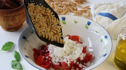 Adding spirals of wholemeal pasta to a bowl with fresh tomato and chopped onion. Stock Footage 195950853