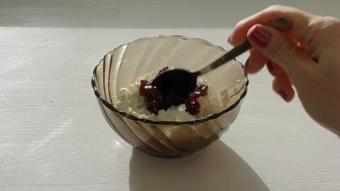 Adding a spoonful of jam in a bowl of cottage cheese on a white background Stock Footage 125521576