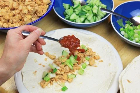 Adding A Spoonful Of Salsa Sauce To A Spicy Chicken Tortilla Wrap. Stock Photos