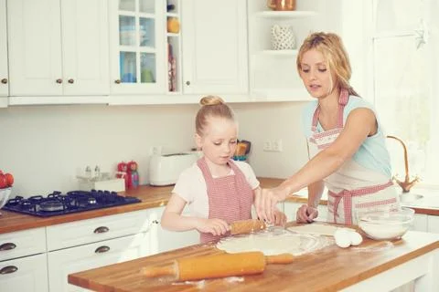 Adding a sprinkle of flour. Cute little girl baking in the kitchen with her mom. Stock Photos