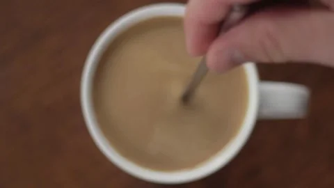 Adding sugar and stirring a hot cup of coffee with milk Stock Footage 332870756