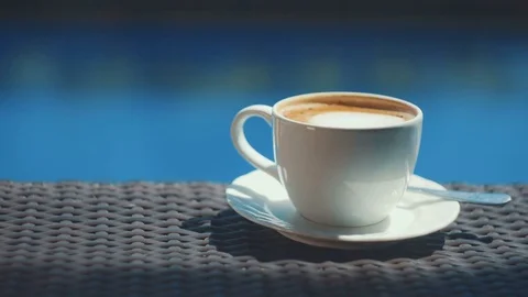 Adding sugar to cup of cappuccino on wicker table with blue water background Video stock 81606476