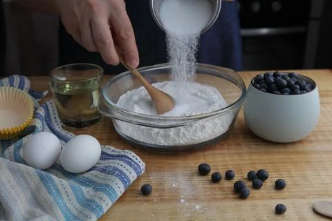 Adding sugar to flour while preparing homemade blueberry muffins Stock Photos