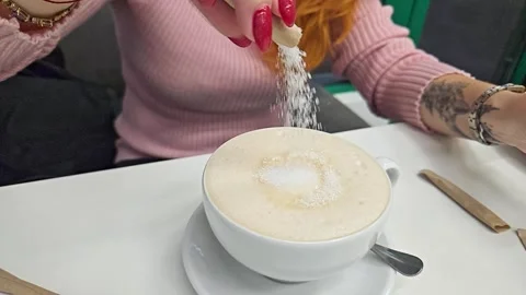 Adding sugar by a girl to a white ceramic latte cup in a restaurant. Slow motion Stock Footage 243025100