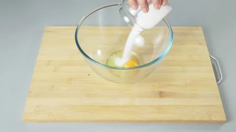 Adding sugar to raw eggs in a bowl before beating them. Preparing dough for Stock Footage 232411151