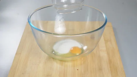 Adding sugar to raw eggs in a bowl before beating them. Preparing dough for Stock Footage 232411295