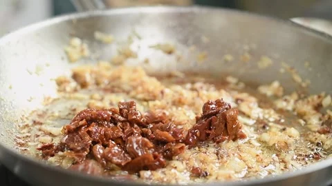 Adding sun dried tomatoes to the chopped onion in a frying pan. Video stock 244386809