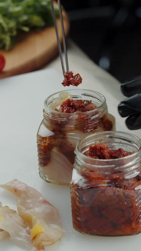 Adding sun-dried tomatoes to jar with smoked fish Stock Footage 308353498