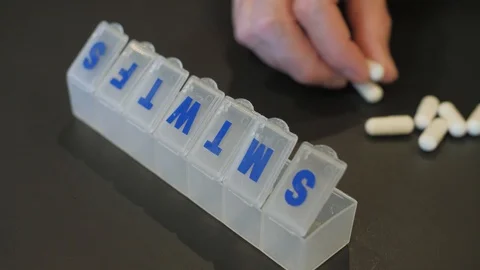 Adding supplement capsules to weekly pill box organizer. Stock Footage 119223612