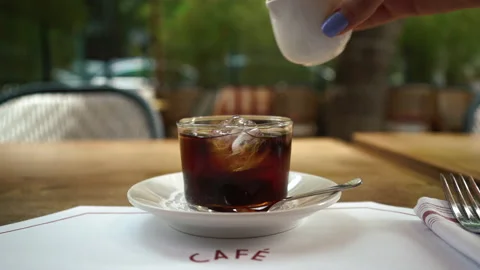 Adding syrup to a cup of black tea. morning coffee outdoors in a cafe in summer Stock Footage 201891616