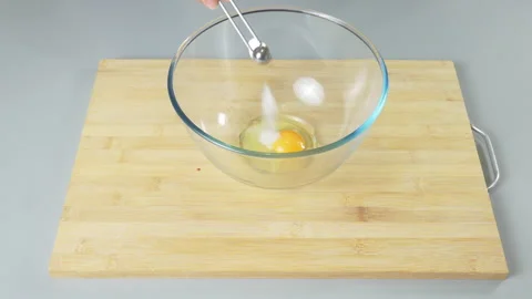 Adding a tablespoon of salt to raw eggs in bowl before beating them. Making Stock Footage 232409082