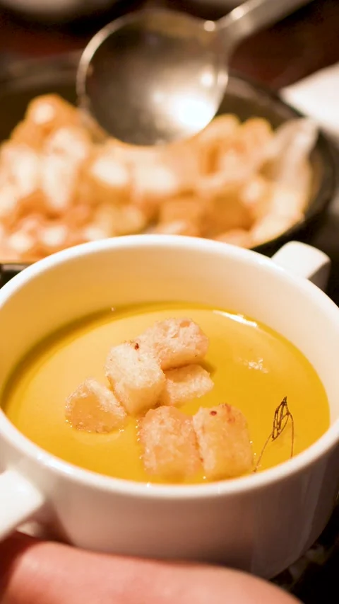 Adding Toasted Bread Croutons to Creamy Pumpkin Soup in White Mug Video stock 335733996