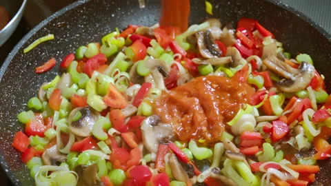 Adding tomato sauce to vegetables that are being fried in a pan. Slow motion 100 Stock Footage 309300443