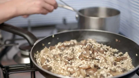 Adding vegetable stock into the mushroom risotto in a frying pan. Stock Footage 134694915