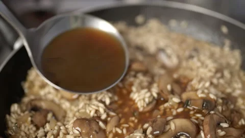 Adding vegetable stock into the mushroom risotto in a frying pan. Stock Footage 134695786