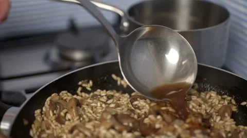 Adding vegetable stock into the mushroom risotto in a frying pan. Stock Footage 134697268